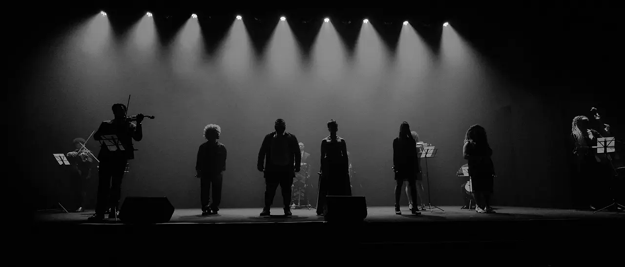 Os músicos da Black SP em silhueta no palco, sob os fachos de luz