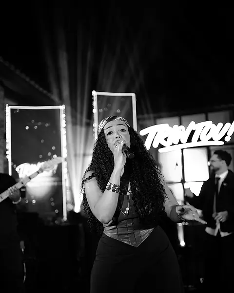 Cantora da Black SP cantando no palco de uma festa de aniversário, contra os fachos de luz