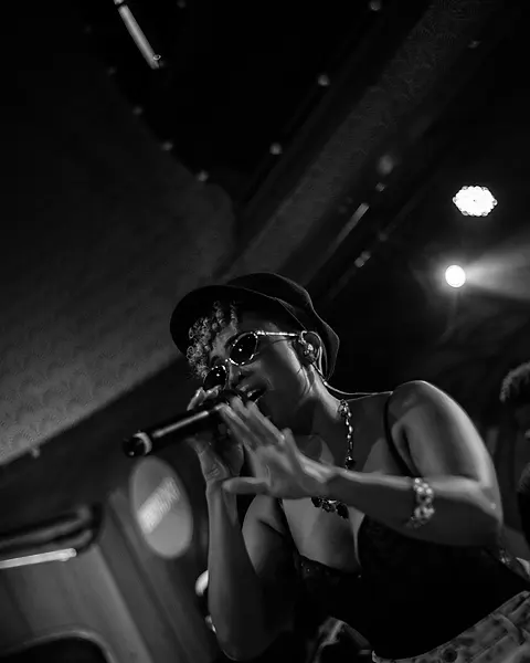 Cantora da Black SP de chapéu e óculos escuros cantando no palco
